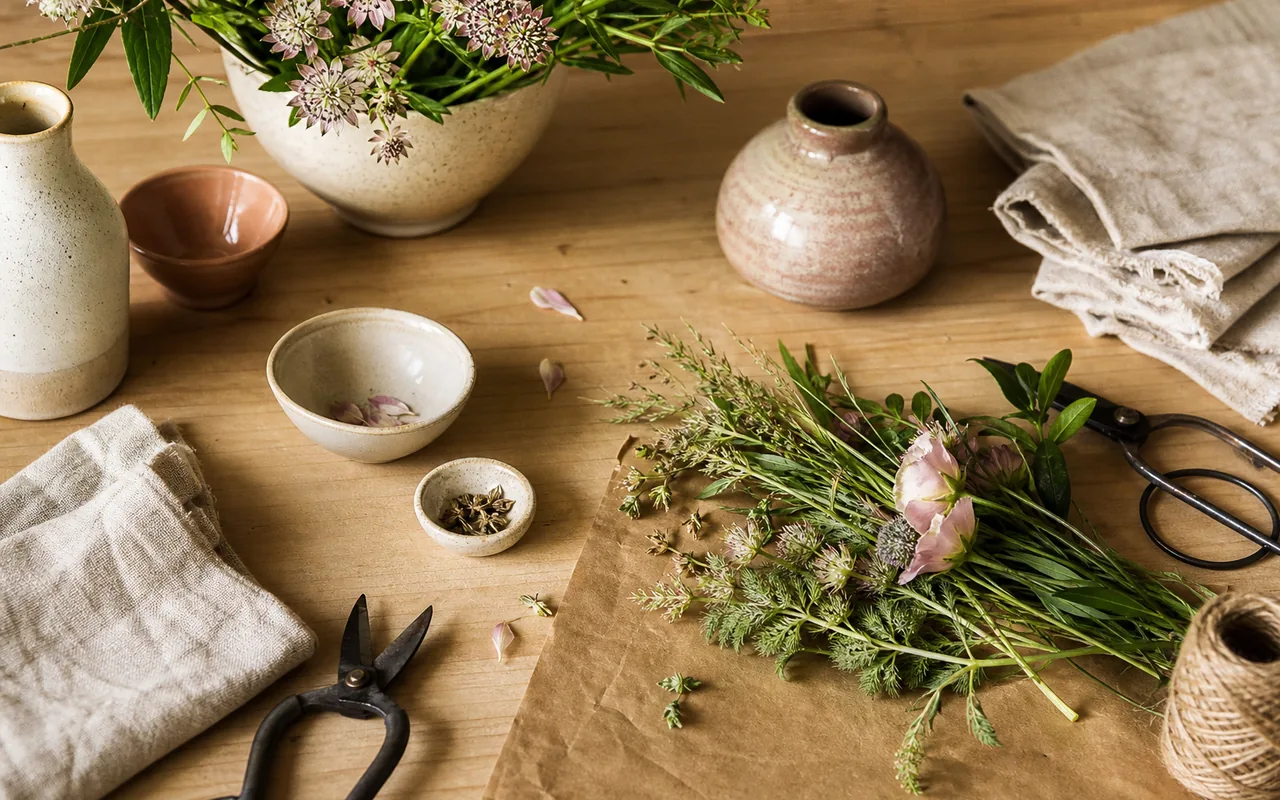 Natural ceramic vessels, plant tools, linen, and botanical materials arranged on a worktable